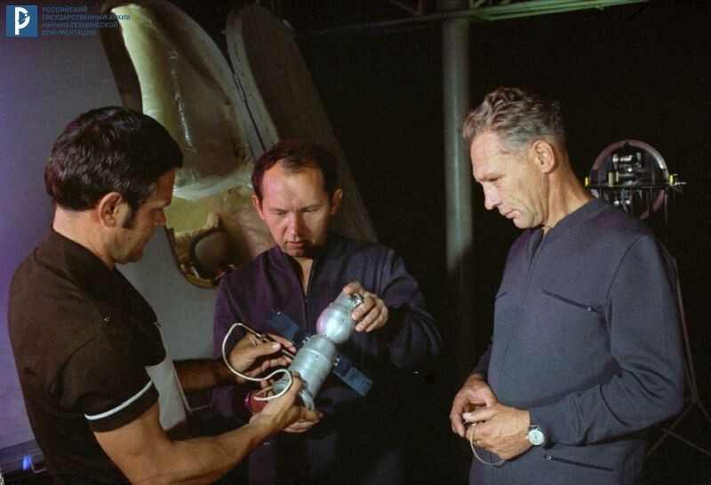 Экипаж космического корабля «Союз-15» – космонавты Л.С. Демин (справа) и Г.В. Сарафанов изучают макет орбитальной станции «Салют» с инструктором ЦПК им. Ю.А. Гагарина. Звездный городок, 1974 г. РГАНТД. Арх. № 0-3762 цв.