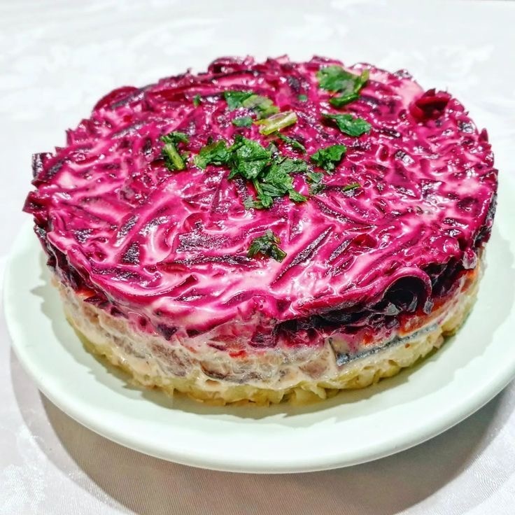 «Селедка под шубой» — это классический слоеный салат, вкус которого напрямую зависит от качества ингредиентов и правильной последовательности слоев.
Основные правила успеха:
Сельдь: Используйте цельную малосольную сельдь, которую нужно очистить самостоятельно. Филе из банок в масле менее предпочтительно [4, 10].
Нарезка: Все овощи лучше натирать на крупной или средней терке. Это делает салат воздушным [4, 5].
Температура: Все ингредиенты должны быть полностью охлаждены перед сборкой, иначе салат быстро испортится [5].
Пропитка: Салату нужно минимум 3–4 часа (лучше ночь) в холодильнике [3, 8].
Классический рецепт (послойно)
Ингредиенты:
Сельдь (филе) — 300–400 г
Картофель — 3 шт. (средних)
Морковь — 2 шт.
Свекла — 2 шт. (крупных)
Яйца — 3–4 шт. (по желанию, классика допускает вариант без них)
Лук репчатый — 1 шт. (маленькая)
Майонез — 150–200 г
Соль — по вкусу
Пошаговое приготовление:
1. Подготовка овощей
Отварите картофель, морковь и свеклу в мундире до полной готовности. Остудите, очистите и натрите на терке в разные емкости [4, 5].
2. Подготовка сельди и лука
Нарежьте филе сельди мелкими кубиками. Лук мелко нашинкуйте. Чтобы убрать лишнюю горечь, лук можно ошпарить кипятком или замариновать в смеси воды и уксуса на 10 минут [2, 5].
3. Сборка слоев (снизу вверх):
Существует два варианта первого слоя: картофель (удерживает структуру) или сельдь (традиционный вкус). Рекомендуется начинать с картофеля.
1 слой: Картофель + тонкая сетка майонеза.
2 слой: Сельдь.
3 слой: Лук (поверх рыбы).
4 слой: Яйца (натертые) + майонез.
5 слой: Морковь + майонез.
6 слой: Свекла. Густо смажьте майонезом и разровняйте [2, 4, 8].
Секрет профессионалов:
Для более нежной текстуры не приминайте слои ложкой, а распределяйте их рыхло. Сетку майонеза лучше наносить из кондитерского мешка или пакета с отрезанным уголком [2, 8].