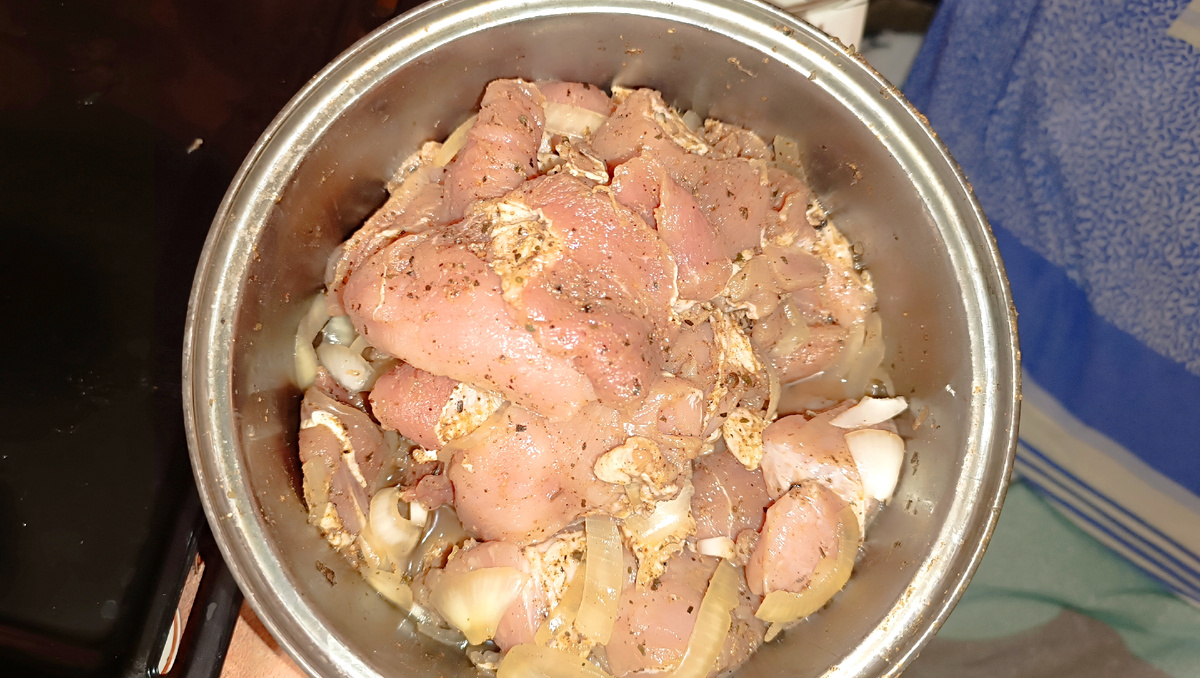 Процесс маринования: крупные куски сырой свинины, смешанные с нарезанным репчатым луком и специями в металлической кастрюле.