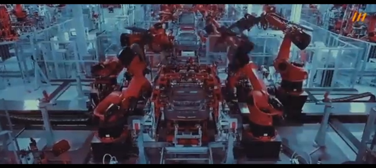 Компьютерная графика. Автомобильный завод Tesla, где роботы собирают машины. Затем кадр с аккумуляторной батареей.