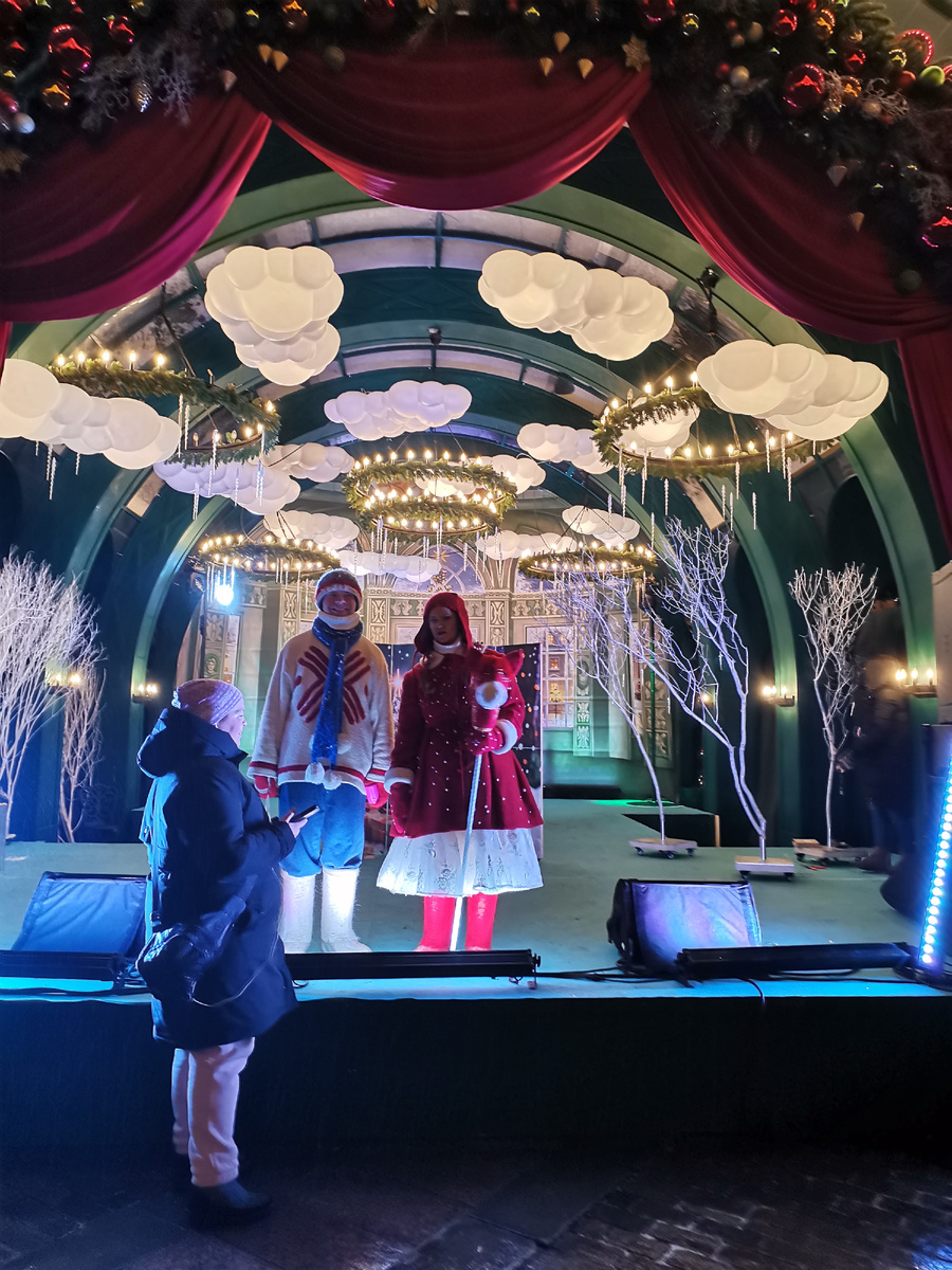 Много искусственного света, мороз, замёрзшие деревья и плотно утеплившиеся от мороза аниматоры на снимке не случайны... Это как предвестие недалёкого будущего с тёмным настоящим и светлым временем, которое прорисовано на заднем фоне и спускается с неба.