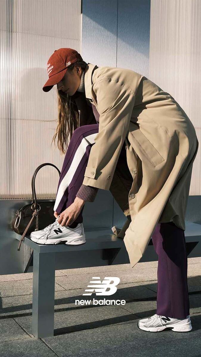 Стильный женский образ 2026 года: серый оверсайз жакет и кожаные брендовые кроссовки на фоне города.