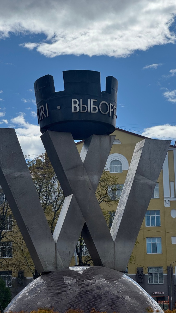 Буква «W» восходит к шведскому названию города, хотя по-фински он называется Viipuri и начинается с буквы «V». В древности, когда использовался скандинавский шведский язык, город звался Wiborg. На гербе города изображена буква «W». Сзади прячется ближайшая к вокзалу пекарня «Хлебник».