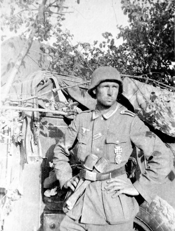 Унтер-офицер вермахта на фоне армейского автомобиля на Восточном фронте. Оригинальная подпись на обороте фотографии — «Ist er nicht lieblich?» (Он не симпатичен?). Каска обернута в нестандартную ткань, нехарактерную для маскировки. Фотография была отпечатана на фотобумаге фирмы «AGFA» марки «Super».