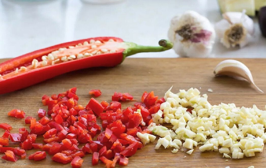 Перец чили очистите от семян и мелко порубите. Зубчики чеснока раздавите ножом и измельчите