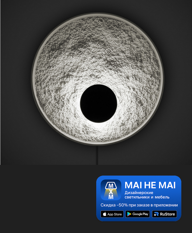 Крупный план круглого белого фактурного настенного светильника с чёрным центром на тёмной стене, внизу размещён синий баннер MAI HE MAI.