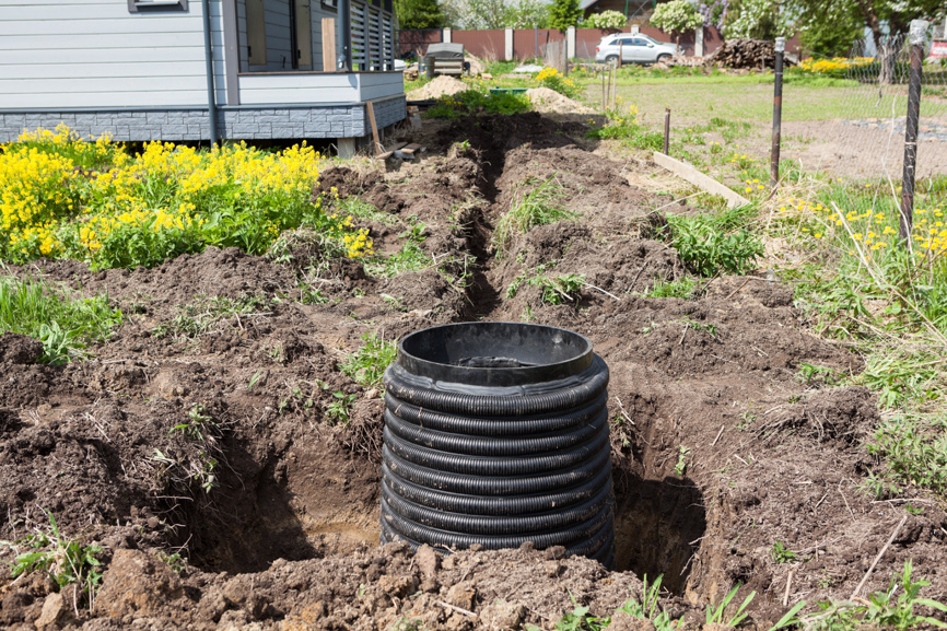 Дренажный колодец для сбора вод на дачном участке, установленный в траншее с трубами