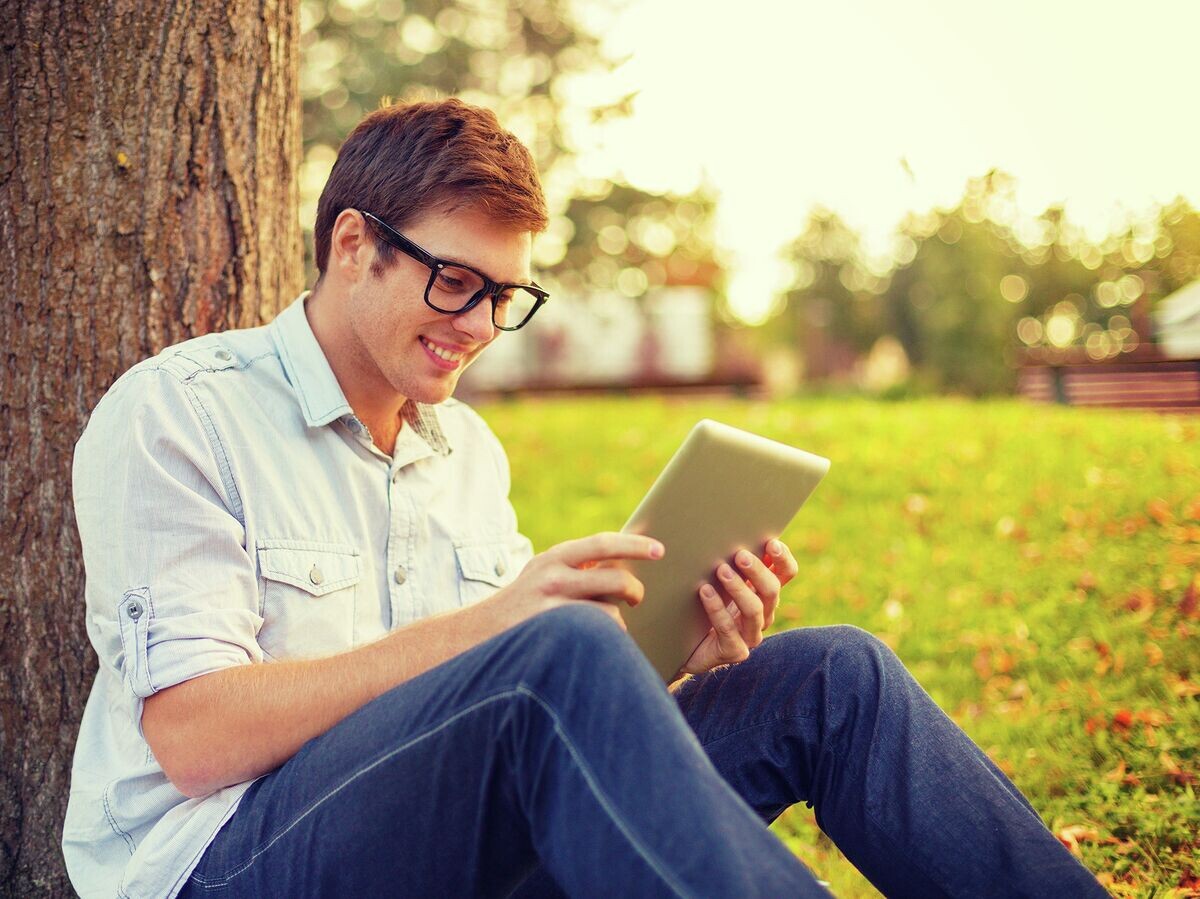    Человек в очках с планшетом в парке под деревом | © Fotolia / Syda Productions