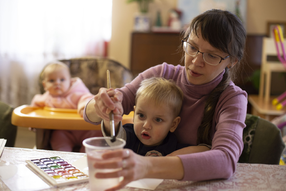 Мама со старшим сыном рисуют. А младшая - внимательно смотрит.