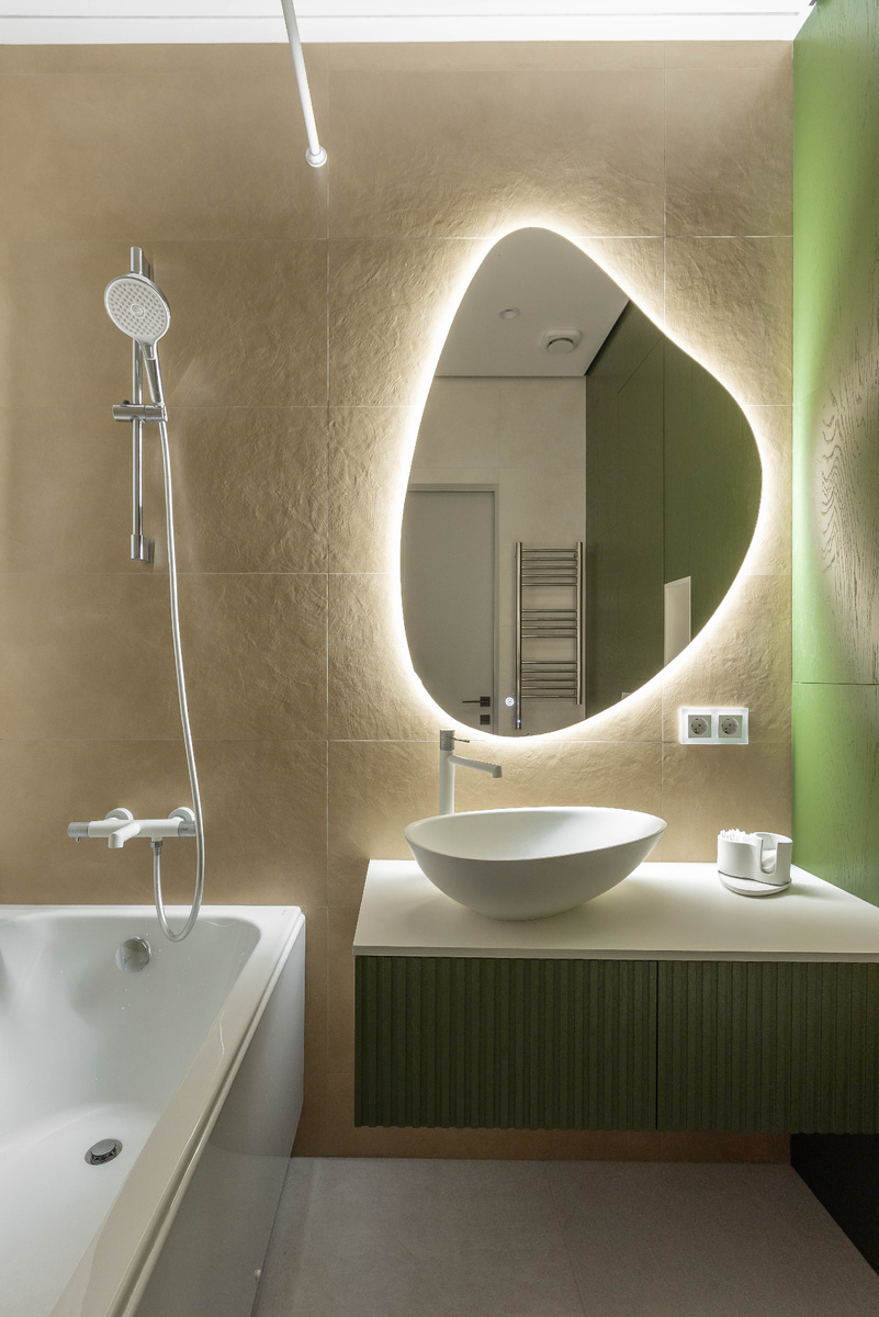 Основной санузел выполнен в светлой гамме с акцентной зеленой мебелью и зеркалом с мягкой подсветкой