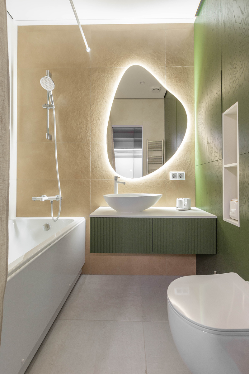 Основной санузел выполнен в светлой гамме с акцентной зеленой мебелью и зеркалом с мягкой подсветкой