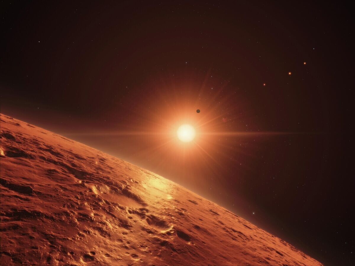    Система планет TRAPPIST-1 | CC BY 4.0 / ESO/N. Bartmann/spaceengine.org / This artist’s impression shows the view just above the surface of one of the middle planets in the TRAPPIST-1 system, with the glare of the host star illuminating the rocky surface (cropped)