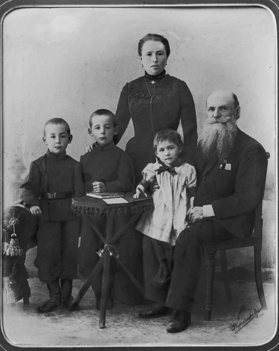 Стоят Саша и Коля. Их сестра Лида сидит на коленях Константина Михайловича Опекушина. На заднем плане стоит его вторая жена - Мария Федоровна Опекушина 