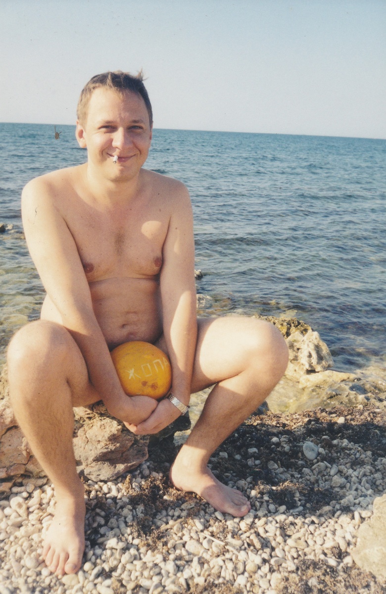 В зубах сигарета в руках дыня. Детских фото с сигаретой не нашел. Слева от уха в море маленькая фигурка видна. Как буд-то кто то тонет и отчаянно машет рукой что бы его спасли. Нет, это просто клякса на фото. Воспринимайте это фото с юмором, без домысливания, пожалуйста.