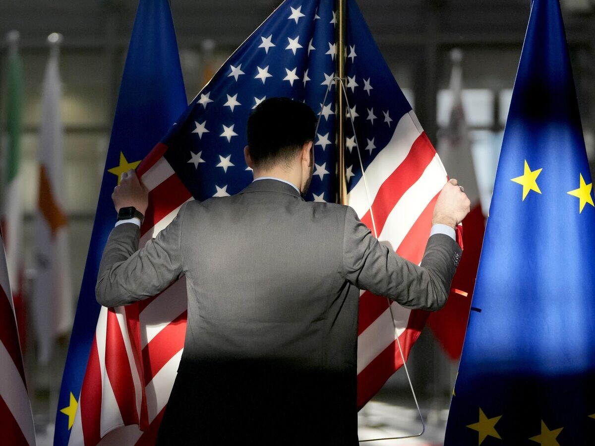    Сотрудник поправляет флаги США и ЕС в здании Европейского совета в Брюсселе | © AP Photo / Virginia Mayo