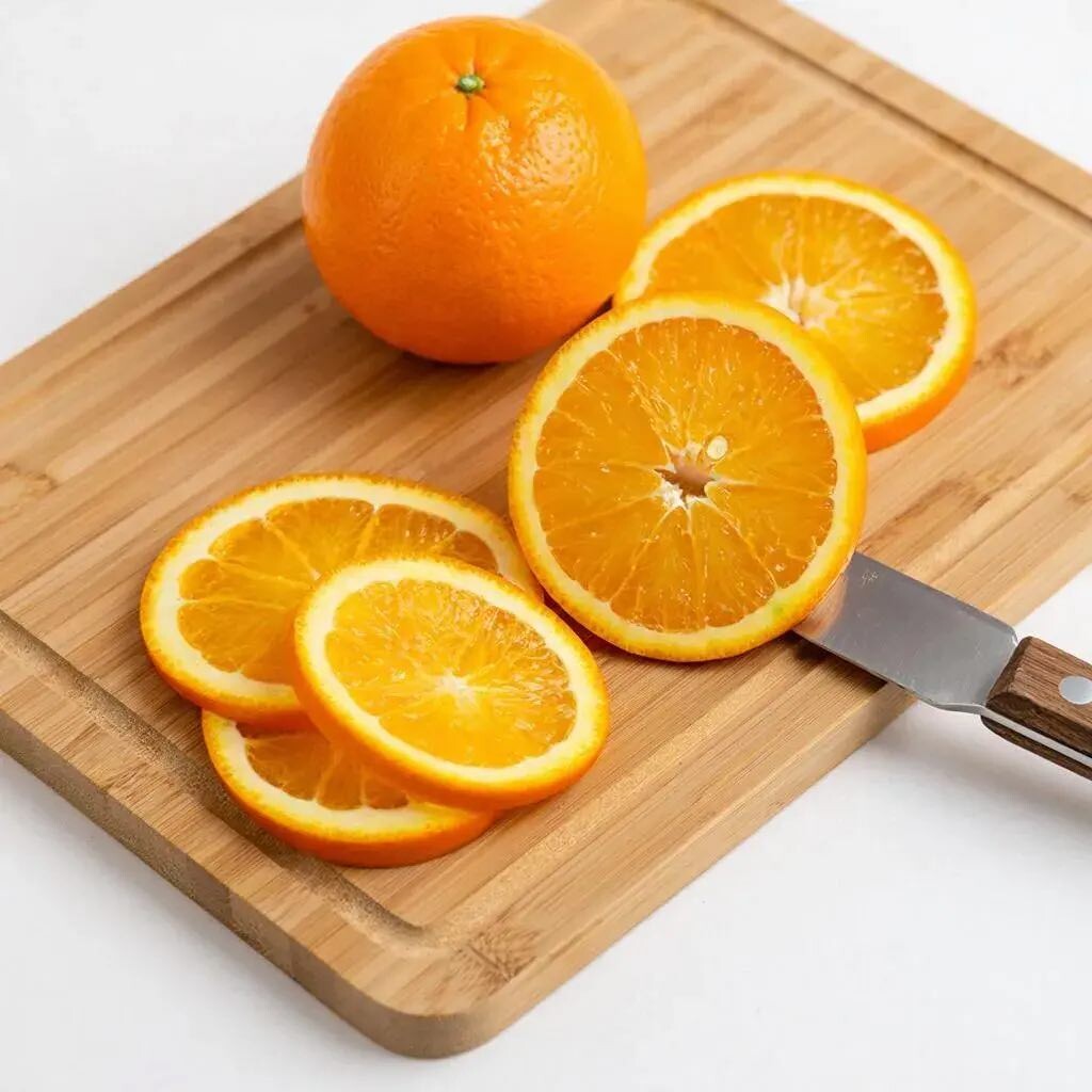 разделочная доска из бамбука, на ней апельсин разрезанный кружочками