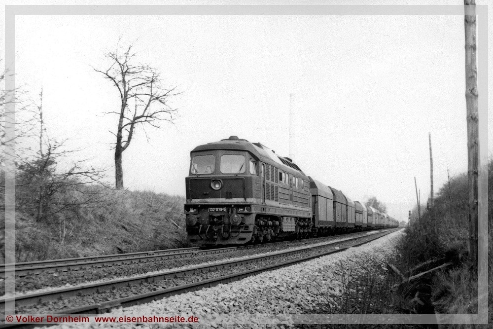 Эта фотография была сделана примерно в 1983/84 году и показывает пустой поезд на прямом участке пути между станциями Кюхвальд и Карл-Маркс-Штадт-Борна. Локомотив 132 079 тянет смешанный состав вагонов типа «Fal». Первые три вагона относятся к типу «Fal-zz» [6556] (до 1971 года: OOt 47, 1972-1979: Fad [6770] и с 1994 года: Fal 162). В ГДР моделисты-железнодорожники могли использовать этот тип вагонов для воссоздания угольных поездов на своих макетах H0 и TT, поскольку эти вагоны-хопперы на тележках, закупавшиеся с 1962 года компаниями Waggonbau Niesky и Waggonbau Gotha, входили в ассортимент миниатюр отечественных производителей. Источник eisenbahnseite.de