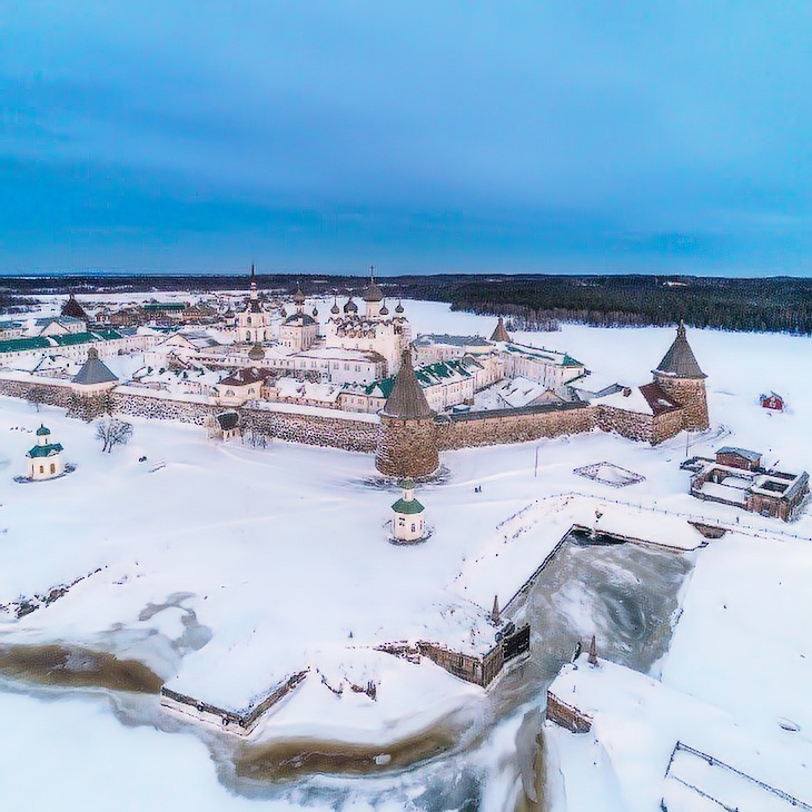  Главный остров Соловецкий с монастырским комплексом XVI века окружен сетью древних монастырских каналов (рукотворных водных путей длиной 30 км). На переднем плане — Секирная гора (99 м) с Христорождественской пустынью и крестом высотой 15 метров. Координаты: 65°02′ с.ш. 35°53′ в.д. Температура воды в августе +12°C, глубина проливов 15-20 метров.