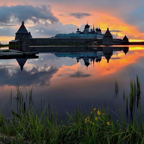   На переднем плане — мраморные плиты с древними резными надписями, возрастом более 400 лет. В лучах заходящего солнца видны уникальные детали архитектуры: астролябии на башнях, каменные кресты и бойницы в форме глаз Воздух наполнен запахом морской соли и можжевельника, температура +18°C.