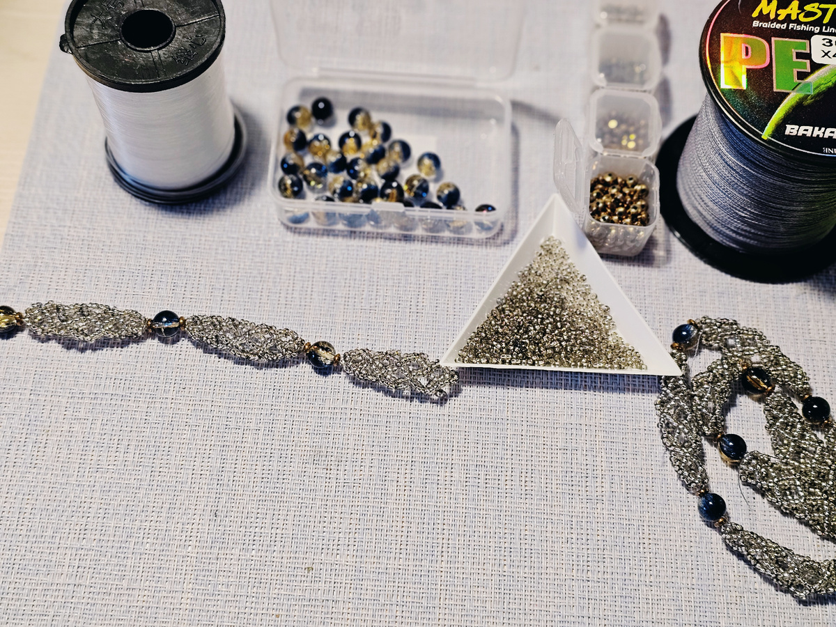 Ажурный эксперимент: от нити до лески. Приветствую, дорогие дрцзтя и коллеги прекрасного! ☕️ Хочу поделиться с вами одним своим исследовательским проектом.Задумала я нежный, ажурный элемент. Его основа — 10 рядов с ячейками на 5 и 7 бисерин, чтобы в итоге получантся кусочек размером около 4 см. Идея в том, чтобы элемент был легким, воздушным, но с четкой геометрией(хотелось жесткости).Испытание материалов:1. На нити 20LB (0.16 мм). Результат — элементы получились невероятно мягкими, пластичными, словно текстильное кружево. Идеально для чего-то объемного и струящегося, что должно мягко ложиться по форме.2. На леске 0.3 мм. Этот образец уже более жесткий, структурный, хорошо держит форму. Чувствуется надежность и четкость.Из таких элементов хочется собрать ожерелье или нежный браслет-боа. А как вам идея с такими элементами сережек?Магия в деталях:В каждый элемент я уже вплела центральную бусину-акцент диаметром 8 мм. Это стекло с потрясающим градиентом: от глубокого тёмно-серого к солнечному желтому. Поверхность — кракле, что добавляет фактуры и винтажного шарма. По бокам бусину подчеркивают рондели из гематита в медной оправе (4*2 мм). Их теплый, землистый блеск прекрасно сочетается с холодным серебром и теплым желтым.Сам ажур плетется из серого прозрачного бисера с серебряной линией — он не перетягивает внимание на себя, а лишь создает мерцающую дымчатую паутинку вокруг бусин.Представляю  — фото с моего рабочего стола (все материалы вживую еще красивее!) и два готовых образца на разной основе. Очень интересно узнать ваше мнение:1. Какой материал, на ваш взгляд, лучше для ожерелья/браслета: мягкая податливая нить или структурная леска?2. Что интереснее будет смотрится: ожерелье из таких элементов, браслет или серьги?Делитесь идеями в комментариях! Возможно, ваша мысль станет решающей для следующего этапа этого эксперимента. 💫А я пока думаю изменить немного конструкцию плетёного элемента или нет?.🤗