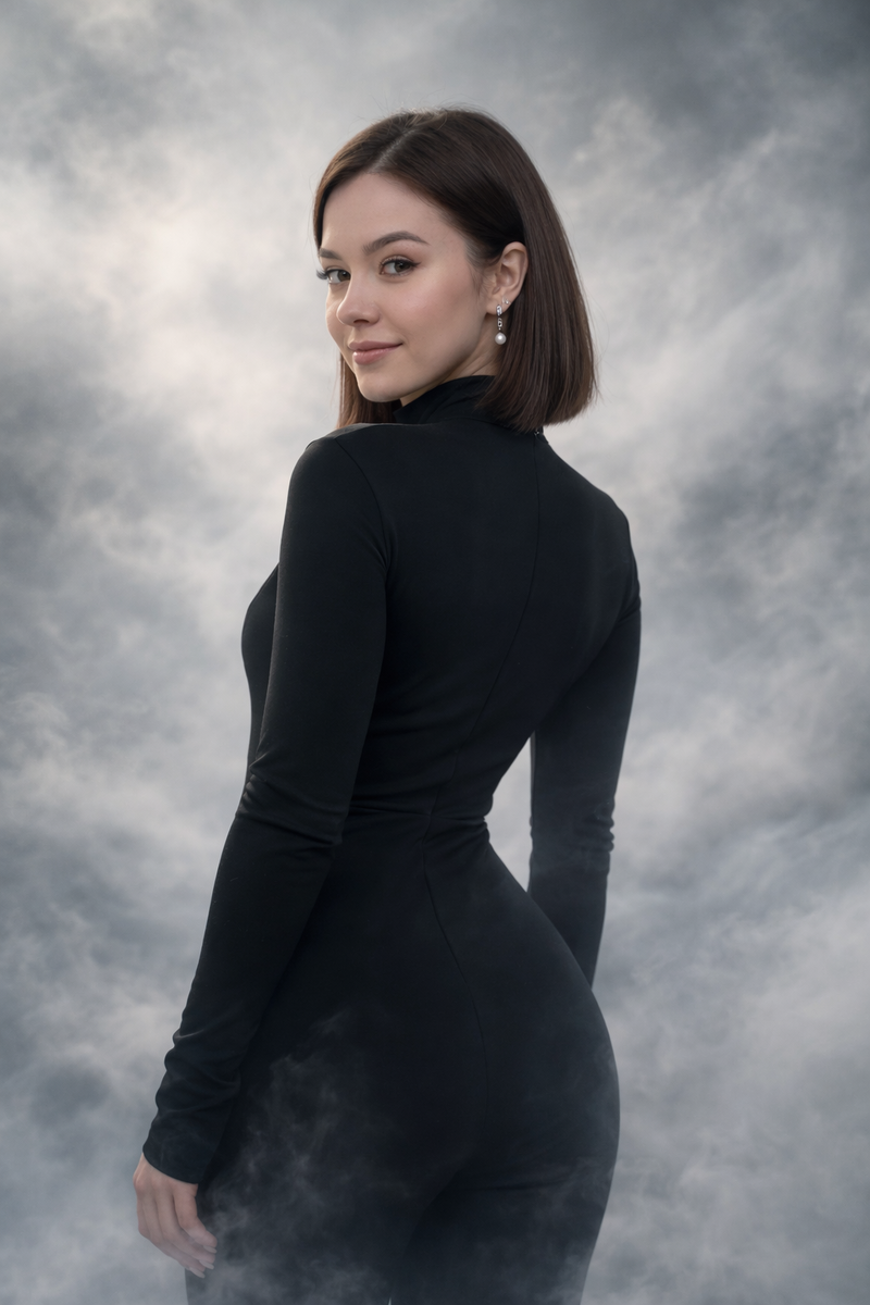 A photorealistic medium shot from behind of a young woman with shoulder-length brown bob hair, wearing a sleek black zip-up jumpsuit. She is standing with her back to the camera and looking over her shoulder directly at the viewer with a slight smile. The background is an abstract, ethereal environment filled with swirling white and light grey mist and fog. Soft atmospheric lighting, magical vibe, high detailed texture, 8k resolution, cinematic composition.