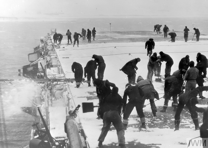 Эскортный авианосец HMS "Кампания" в Мурманске, готовится к отплытию с возвратным конвоем в Великобританию. За время стоянки корабль присыпало снегом, поэтому 
матросы взялись за снегоуборочные лопаты.