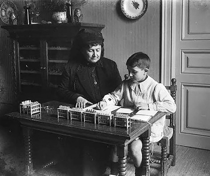 Мария Монтессори и ученик начальной школы занимаются математикой