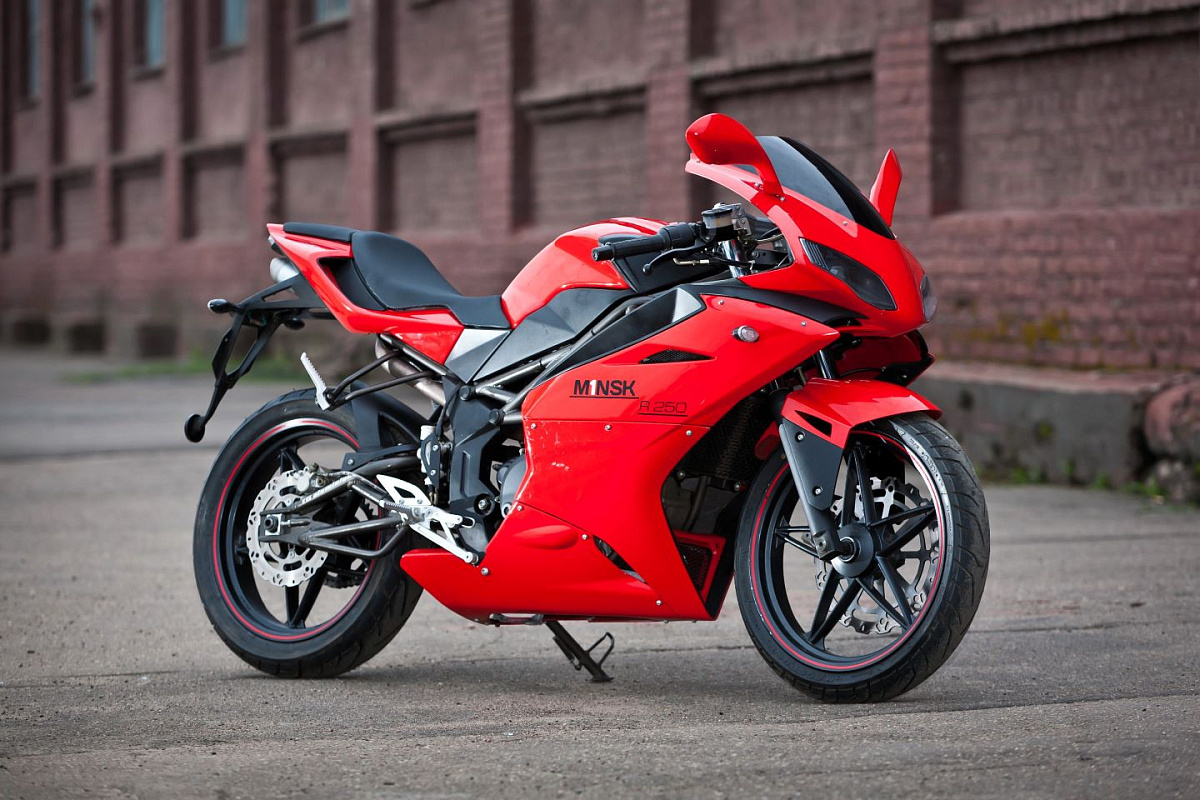 Лёгкие мотоциклы «Минск» ценились за дешевизну и надёжность. И пускай они никогда не считались «крутыми», всё равно их любили. Даже сейчас про «Минчики» вспоминают, мечтая, что их когда-нибудь возродят.Увы, завод Мотовело был объявлен банкротом в 2018 году. То, что сейчас продаётся под этим брендом, собирает уже другое юридическое лицо. Конечно, примерно с 2011 года, предприятие начало выпуск китайских моделей под своим именем. Но это не совсем та схема, что популярна сейчас. Там ещё имелись конструкторы, выбиравшие лучшие технические решения. Да и мотоциклы разрабатывали не китайцы, а более известные бренды.Поэтому байки, собранные на заводе «Мотовело» в период с 2011 по 2015 годы, считаются лучшими. Да, они китайские, но даже сейчас, когда прошло более 10 лет, они радуют своих владельцев, далеко уже не первых. И сегодня редакция carsweek.ru расскажет про самый интересный серийный мотоцикл, когда-либо выпущенный «Мотовело» – это стильный спортбайк Минск (M1nsk) R250.История появленияМинск R250 сделан в Китае, но, по факту, является международной разработкой. Проектировали спортбайк в Европе конструкторы британской компании Megelli. Они как раз специализируются на малокубатурных моделях.Сейчас уже сложно сказать, разрабатывали Минск R250 для «Мотовело», или нет. Одно точно известно – у этого байка есть «брат-близнец», который называется Megelli R250. Эта модель продавалась не только в Европе, но и в Японии, что уже намекает на качество сборки и надёжность.Двигатель китайский, но и его разрабатывали не в Поднебесной. Мотор итальянский, так что он «породистый».Возвращаясь к «Мотовело», стоит отметить, что в период с 2007 по 2010 годы завод, попавший в частные руки, пережил масштабную модернизацию. Полностью не отказываясь от старых моделей, было решено вывести на рынок сразу несколько новых байков. Спортивным из них стал Минск R250.Причём это полноценный внешне спортбайк. Да и мотор у него жидкостного охлаждения, так что техника бодрая, рассчитанная на высокие обороты