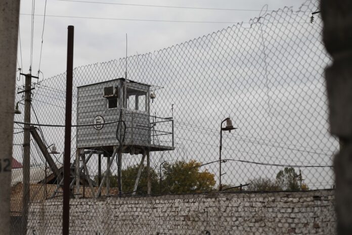    Логотип цифровой пенитенциарной системы, взломанный через традиционные аналоговые техники, символизирующие уязвимость современных технологий.