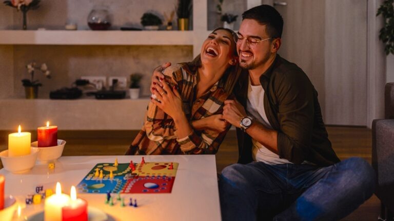    A man and his girlfriend are sitting in a dark room caused by an electric crisis and a blackout and playing a board game.