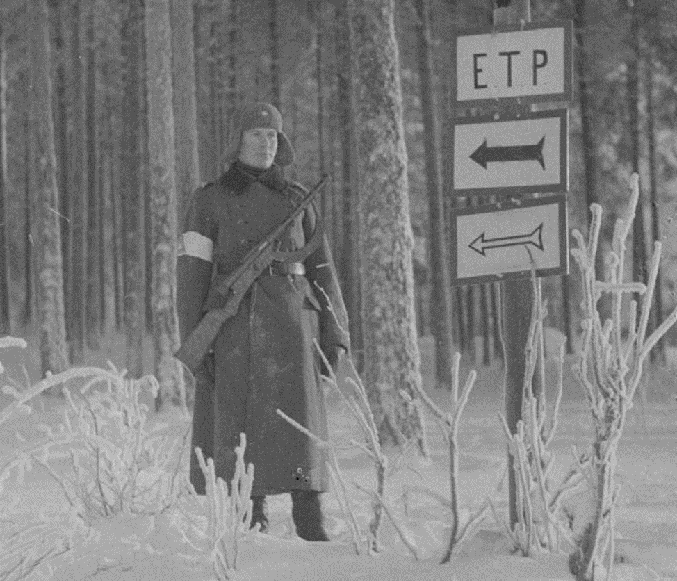 Часовой учебного центра снабжения в Мянття с пистолетом-пулеметом «Суоми» M/26. Дорожный знак ЭТП рядом с ним – это точка снабжения продуктами питания. Снято в январе 1942 года. Взято с сайта https://topwar.ru/194094-svoe-i-chuzhoe-pistolet-pulemet-suomi-m26.html