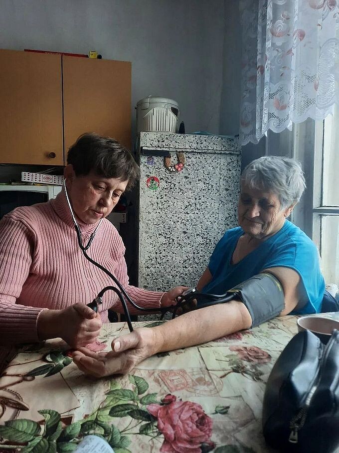 Социальный работник измеряет давление пожилой женщине