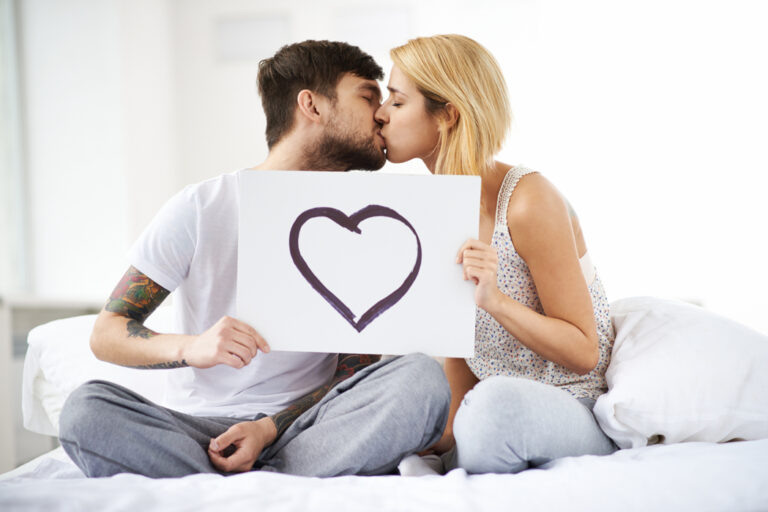    Kissing cool couple holding sheet of paper with heart depicted on it