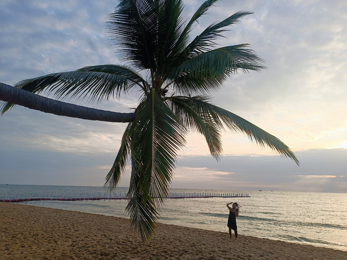 Море и пальмы и мечтательница с морской раковиной у уха
