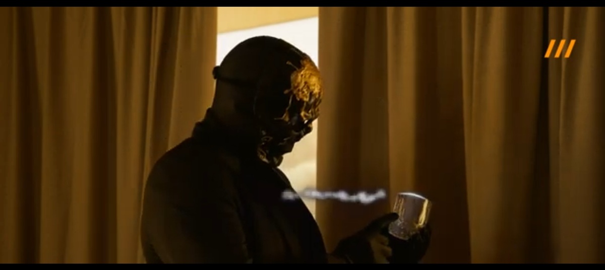 Мориарти стоит в комнате, держит в руках хрустальный стакан, объясняя свойства предмета.