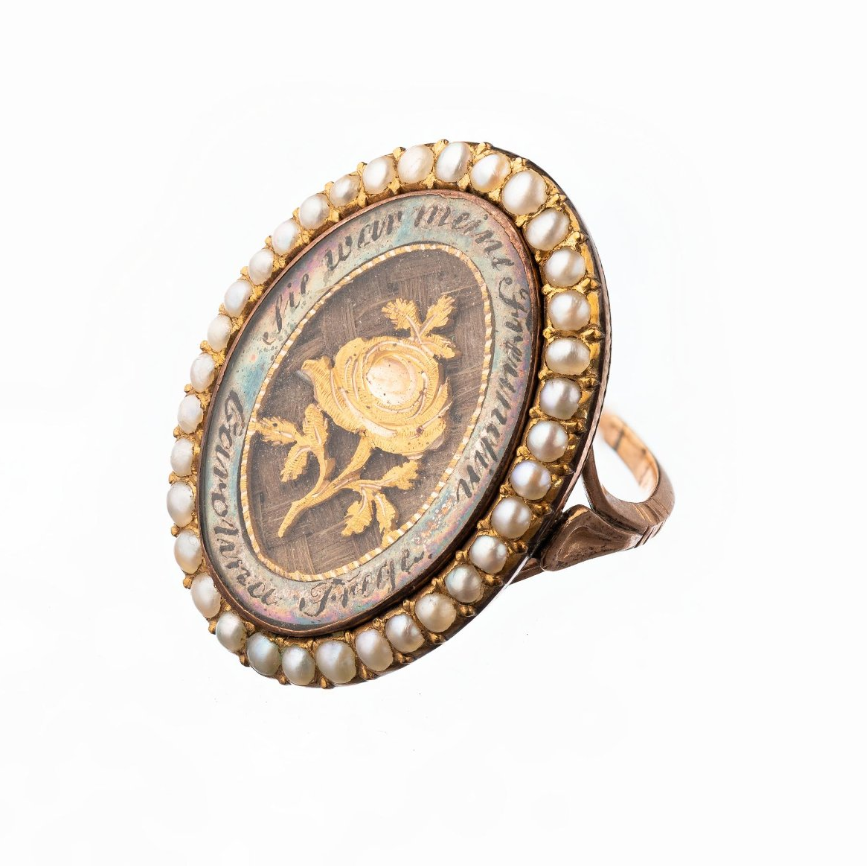 Кольцо. Россия (?). 1789 г. Золото, жемчуг, кость, стекло, волосы, перламутр. Размер: 2,7×2,3×2,1 см. На щитке кольца — надпись: «Carolina Freqe sie war meine Freundin» (Каролина Фрэк. Она была моей подругой).
