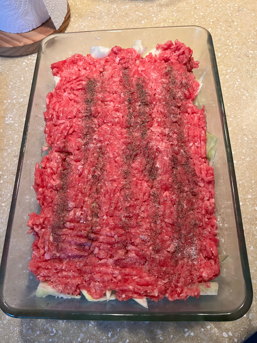 Под слоем фарша, присыпанным черным перцем, лежит слой капусты 