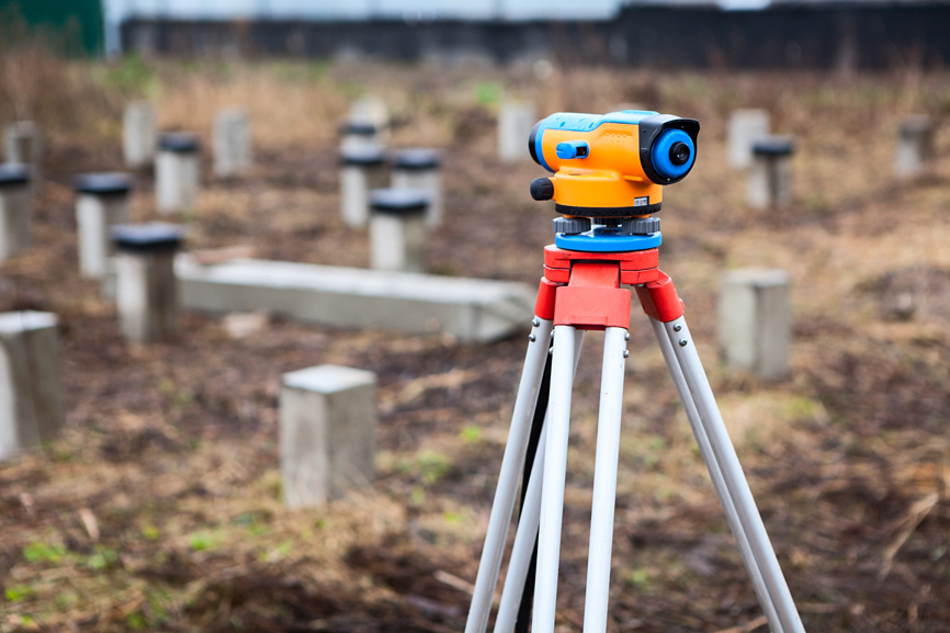 Геодезический прибор на треноге для измерения границ участка на открытой местности