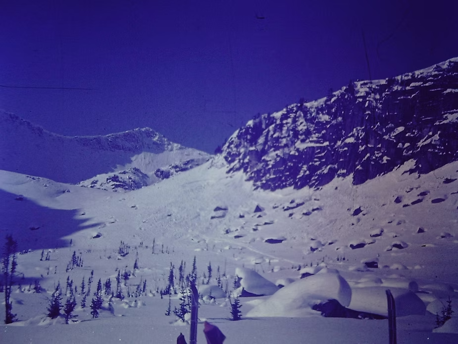 На слайде видна лыжня на склоне и вверху под скалами  отрыв лавины.