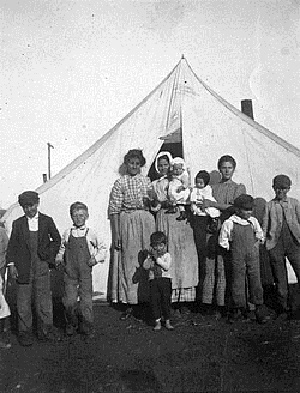 Три жены шахтера и их дети у входа в палатку.