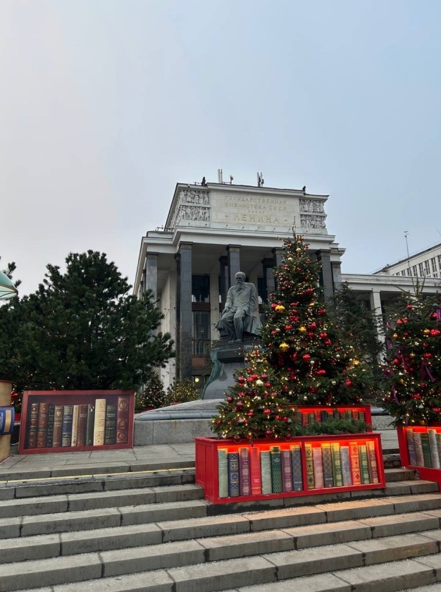 Куча елок, украшены и оформлены под тему книг. На фоне - библиотека