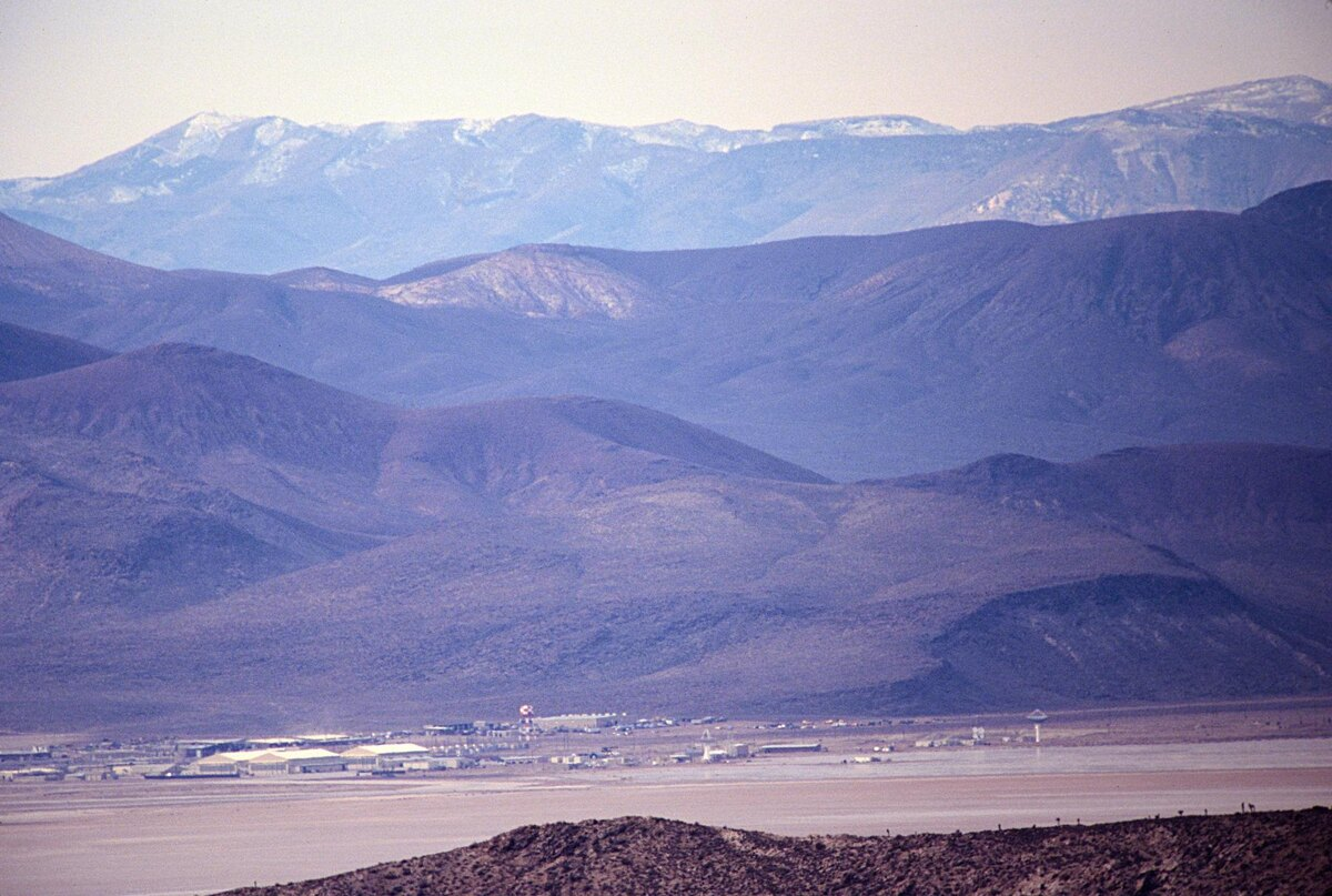 Вид на Зону 51 с соседнего горного хребта — ближе не взять. На дне высокого озера Грум-Лейк едва различам комплекс зданий. Именно отсюда, с максимально допустимого расстояния, энтузиасты годами пытаются разглядеть, что происходит внутри периметра.