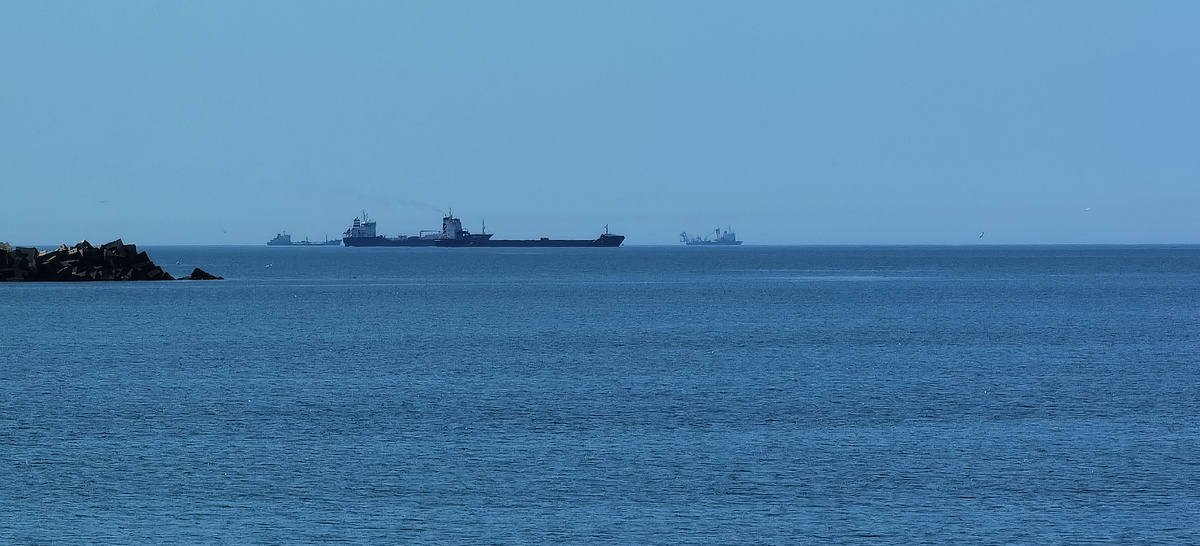 Корабли на рейде в ожидании очереди для захода в залив по проливу между двумя молами