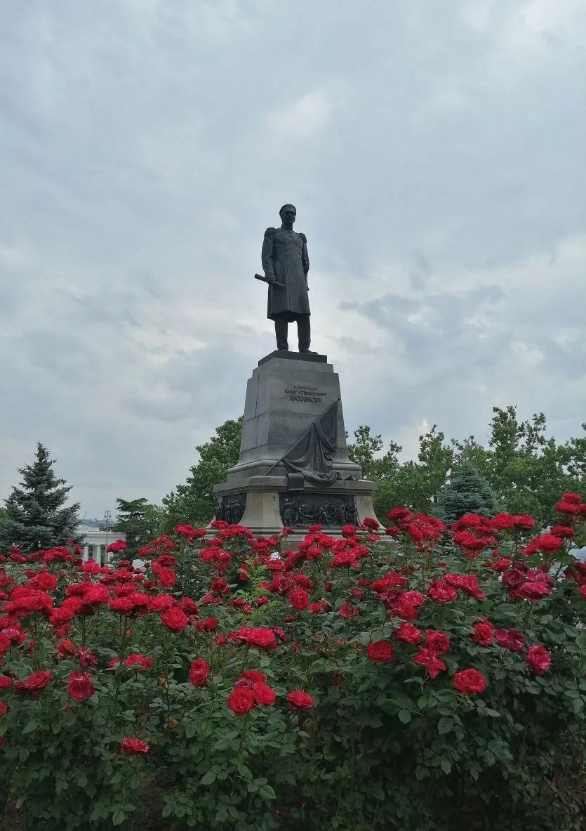 Площадь Адмирала П. С. Нахимова в Севастополе, утопает в розах. На первом плане памятник Нахимову, вдали немного видна колоннада Графской пристани