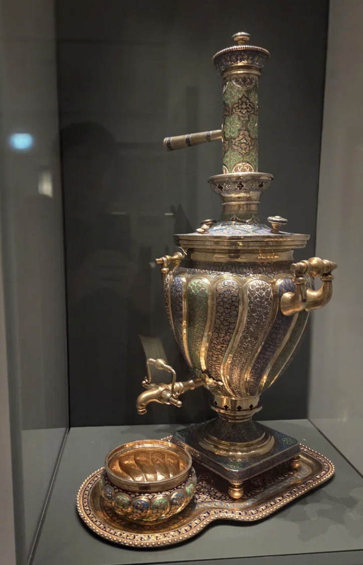 Самовар, поднос и чаша, Центральная Азия, Бухара (1910 год) Серебро, эмаль; золочение, гравировка, чернь, чеканка Самовар: высота 57 см Поднос: длина 45,5 см, ширина 28,8 см
Чаша: высота 7,3 см, диаметр 13,8 см