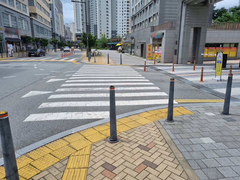 Материалы: клинкер/брусчатка в зоне перехода, резиновые или полиуретановые болларды, пониженные бордюры 0–2 см, контрастные тактильные плиты