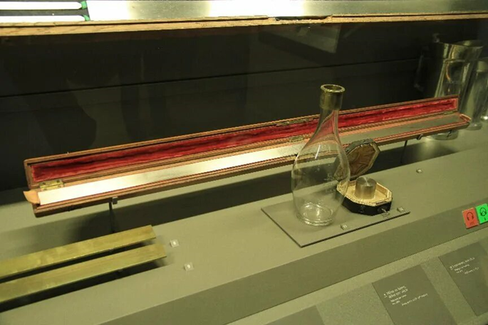 Оригинальная метровая линейка - эталон, выставленная во Французском музее искусств и ремесел. Перед линейкой находятся: эталонная стеклянная бутылка объёмом ровно один литр; и эталонный грузик весом ровно один килограмм.