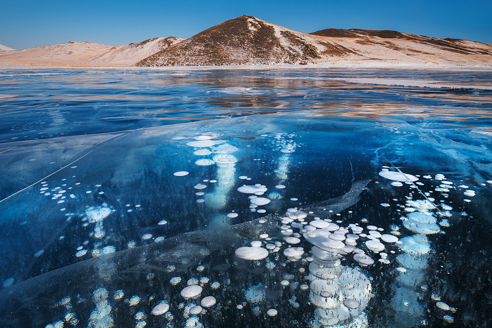 Озеро Байкал зимой покрытое льдом и сияющее голубыми бликами.