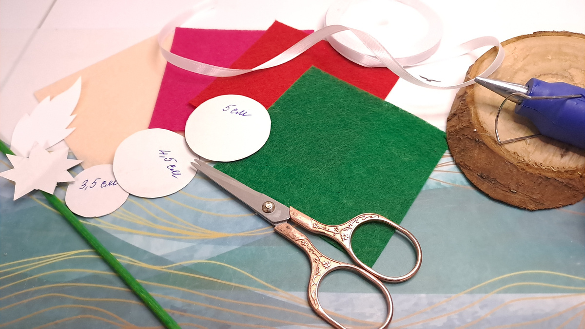 Все необходимое для создания розочек из фетра: шаблоны, ножницы, пистолет для клеея со стержнем, фетр, лента, опора для растений (можно заменить шпажками) и лента.