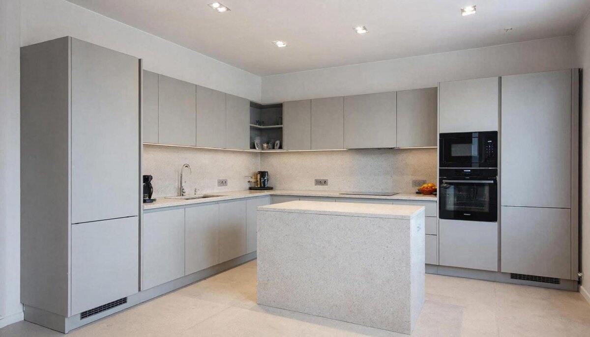  Современная кухня на заказ с угловой планировкой, матовыми светло-серыми фасадами и кварцевой столешницей. Встроенная техника скрыта, нет щелей, много естественного света.